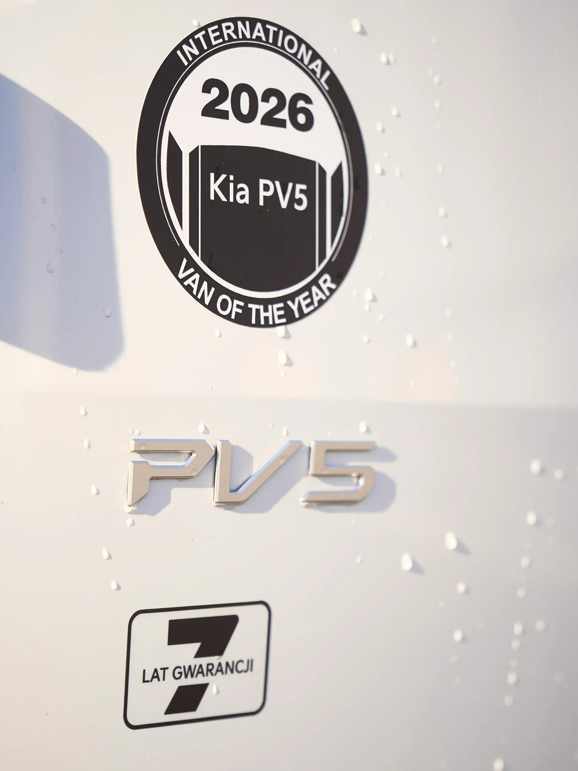 Znaczek PV5, naklejka International Van of the Year 2026 i oznaczenie 7 lat gwarancji na nadwoziu z kroplami wody