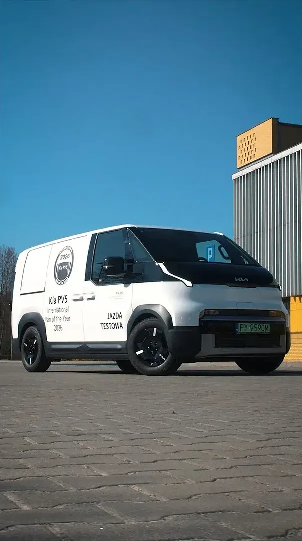 Pionowy kadr z materiału wideo: Kia PV5 przed nowoczesnym budynkiem