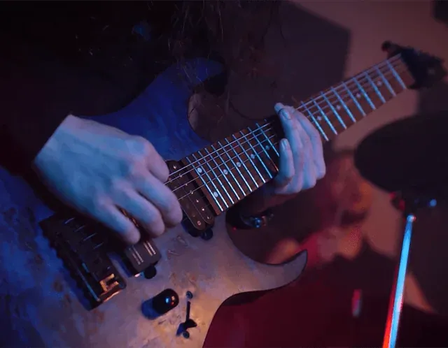 Dłonie grające na gitarze elektrycznej w niebieskim i czerwonym świetle